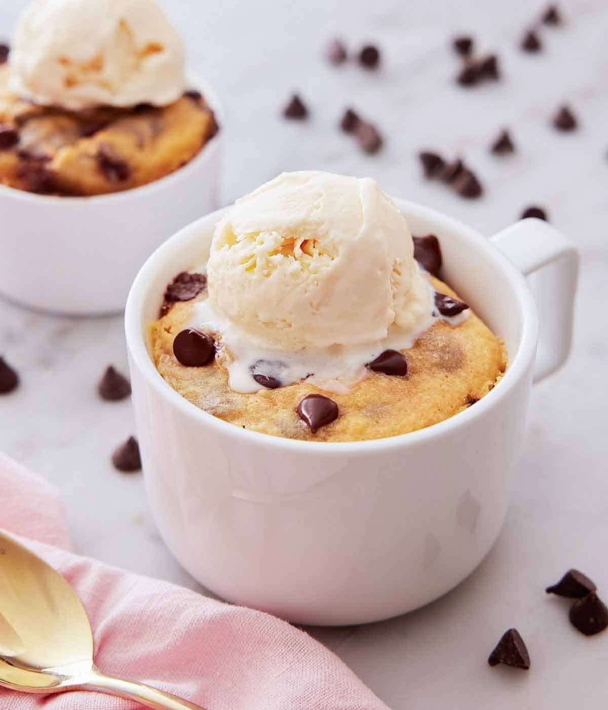 A cookie in a mug with a scoop of vanilla ice cream on top.