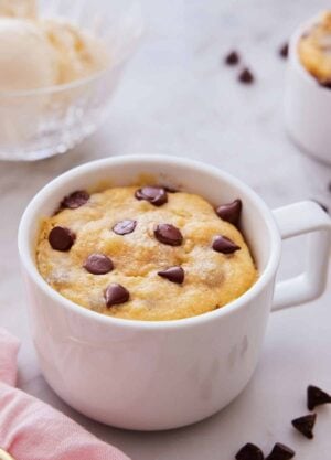 A cookie in a mug with chocolate chips scattered around.