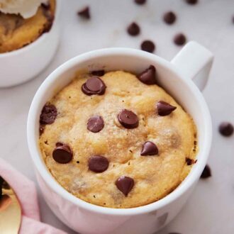 Pinterest graphic of an overhead view of a cookie in a mug with chocolate chips scattered on the counter.