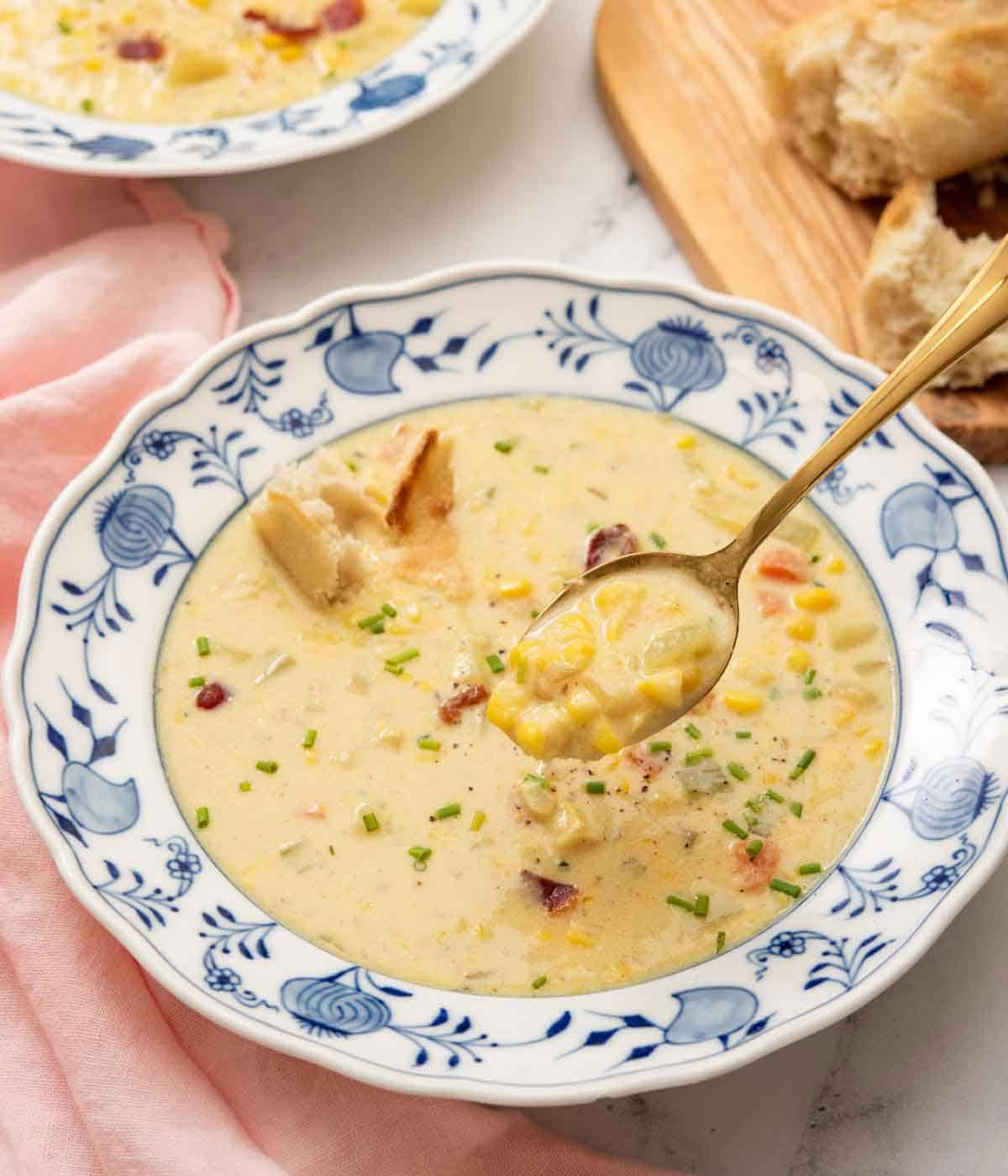A bowl of corn chowder with a spoonful lifted up.