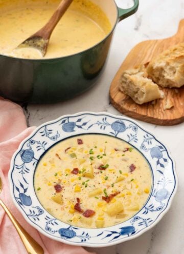A bowl of corn chowder with a green dutch oven with more chowder in the background.