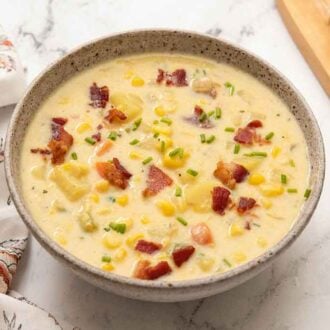 A bowl of corn chowder with fresh chives and crispy bacon bits as garnish.