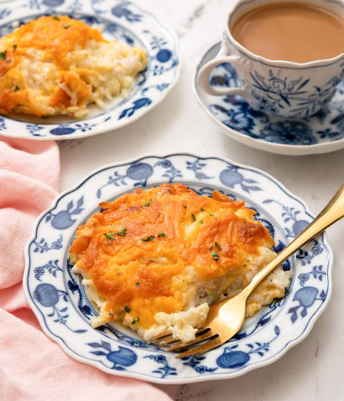 A plate with a serving of hashbrown casserole with a fork tucked in.