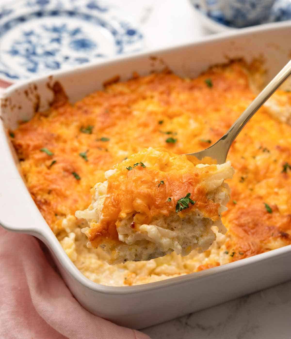 A spoonful of hashbrown casserole lifted from a baking dish.