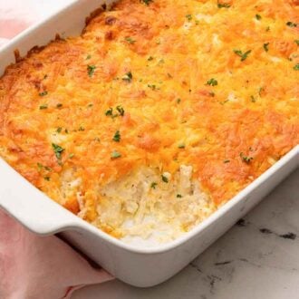 A white baking dish filled with hashbrown casserole with a portion scooped out.