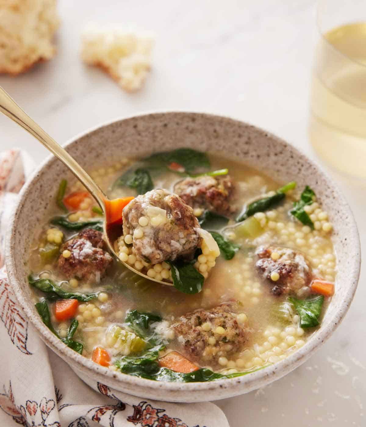 A bowl of Italian wedding soup with a spoonful with a meatball lifted out.