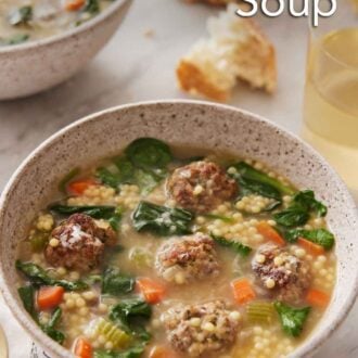 Pinterest graphic of a bowl of Italian wedding soup with a glass of wine and torn bread in the background.