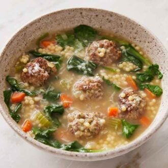 A bowl of Italian wedding soup with some torn bread in the background.