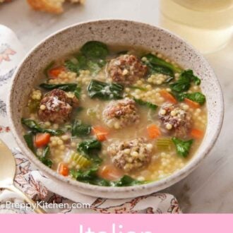 Pinterest graphic of a bowl of Italian wedding soup with a glass of wine and some bread in the background.