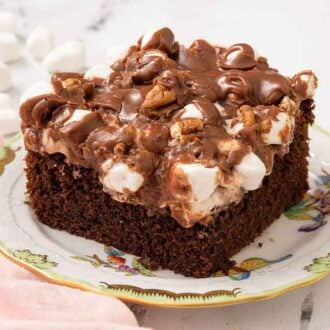 A plate with a square slice of Mississippi mud cake with mini marshmallows scattered around.