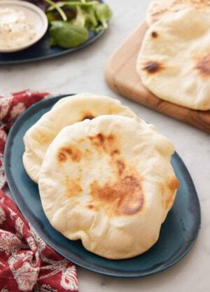 A blue platter with two pita bread on it with more in the background.