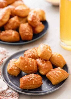 A plate of pretzel bites with a platter of more pretzel bites and a tall glass of beef in the back.