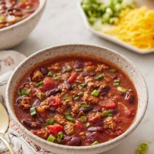 A bowl of slow cooker chili with toppings in the background, out of focus.