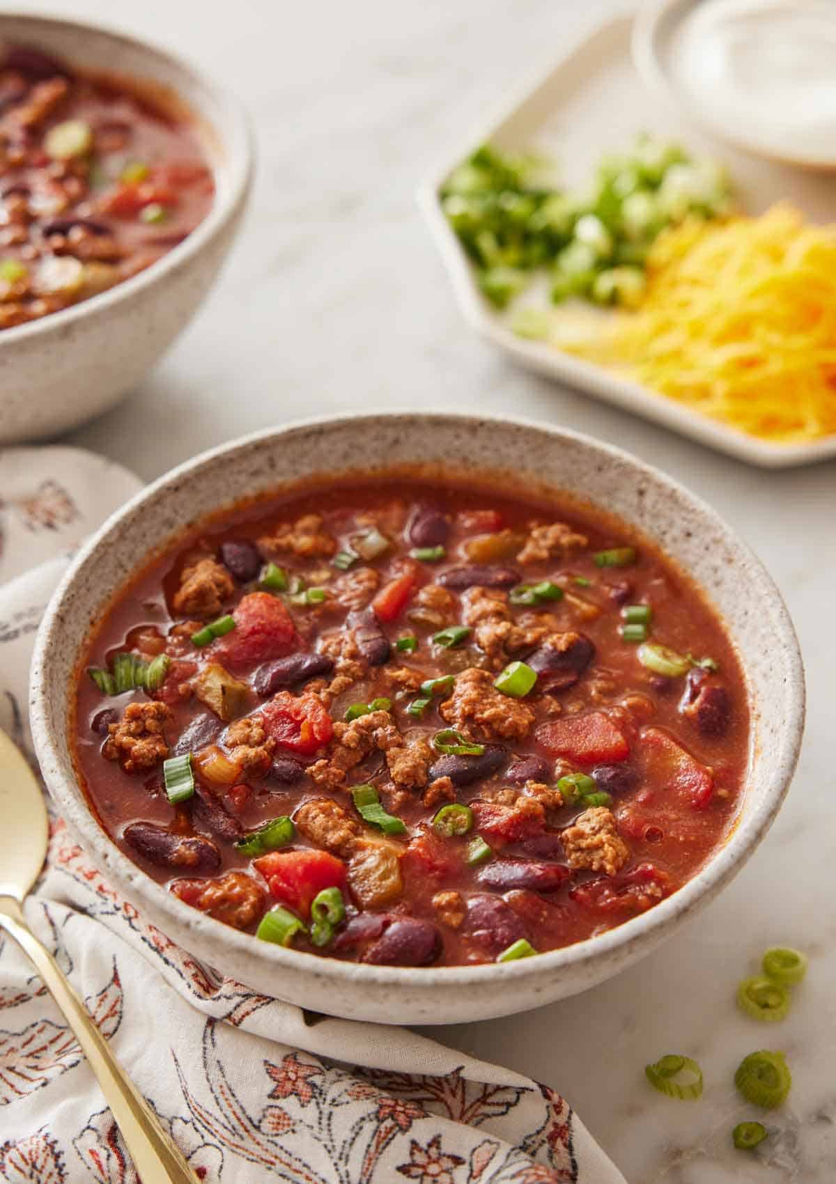 A bowl of slow cooker chili with toppings in the background, out of focus.