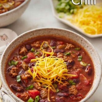 Pinterest graphic of a bowl of slow cooker chili with shredded cheddar cheese on top.