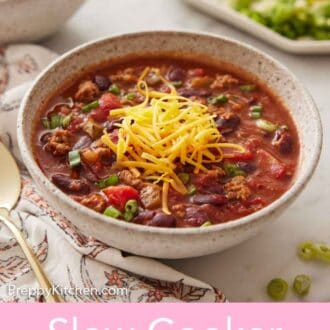 Pinterest graphic of a bowl of slow cooker chili with shredded cheese on top with toppings in the background.
