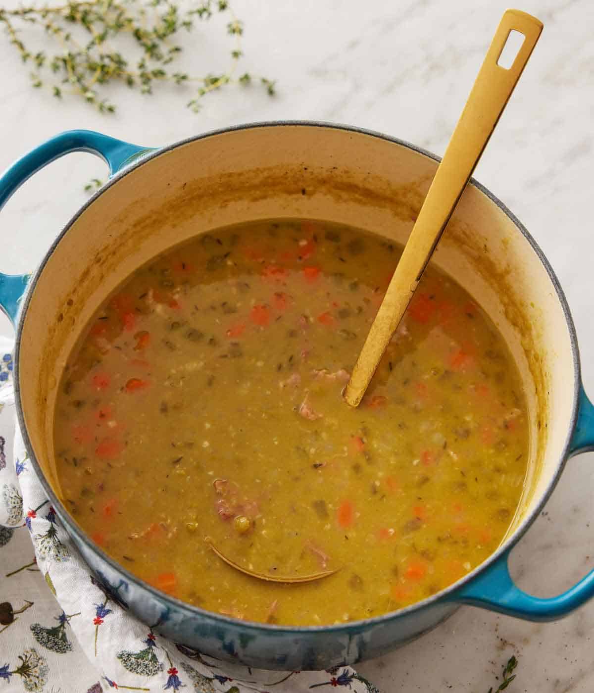 An overhead view of a pot of split pea soup with a ladle inside.