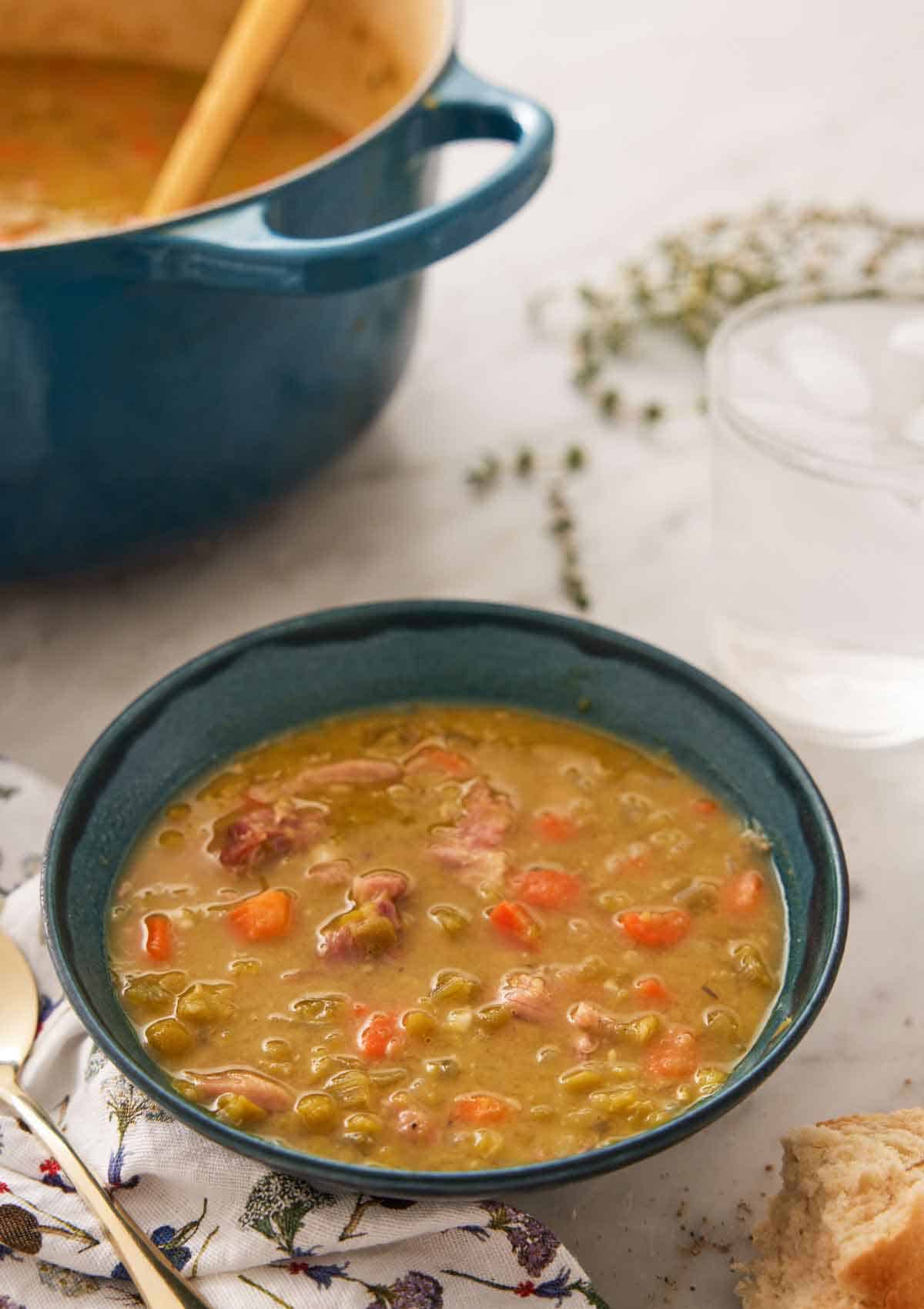 A bowl of split pea soup with a glass of water in the back along with a blue pot.