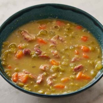 A blue bowl of split pea soup with pieces of shredded pork inside.
