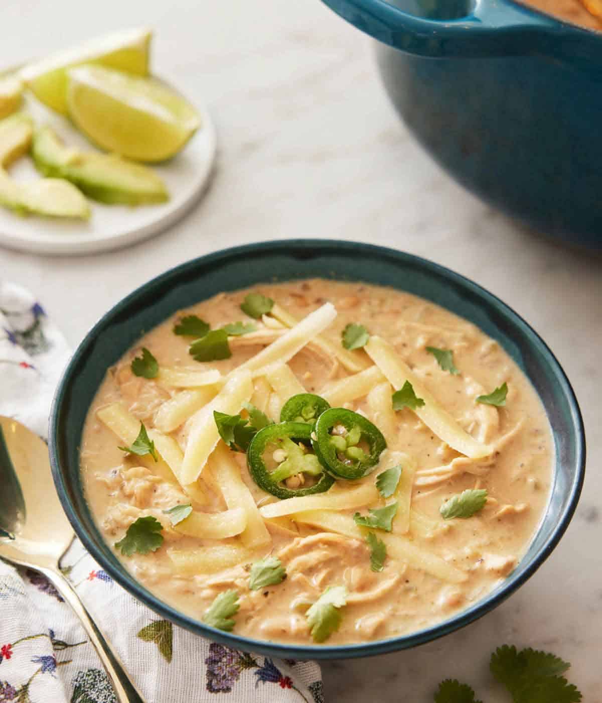 A bowl of white chicken chili with some sliced jalapeno, cilantro, and shredded cheese on top.