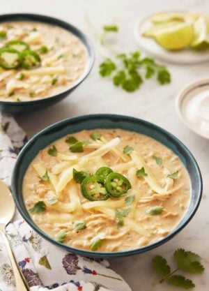 A bowl of white chicken chili with sliced jalapeno and shredded cheese on top.