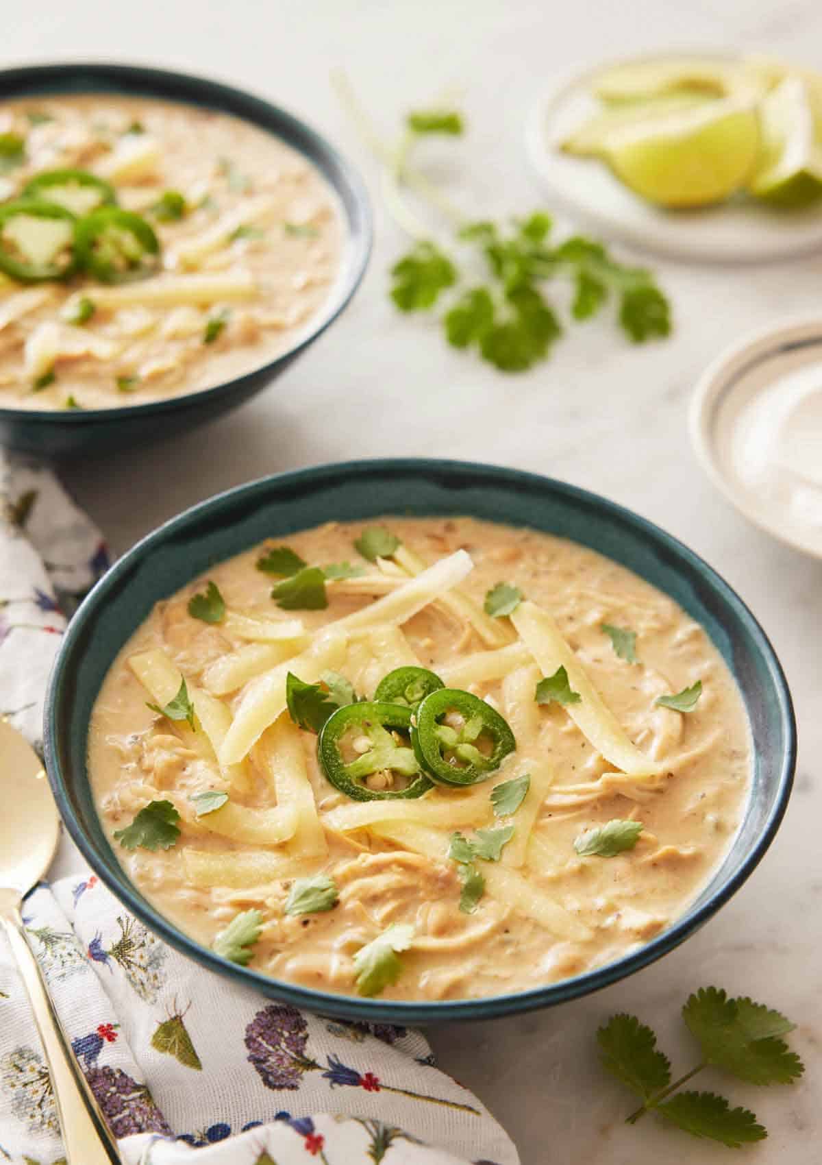 A bowl of white chicken chili with sliced jalapeno and shredded cheese on top.