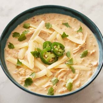 A bowl of white chicken chili with shredded cheese, sliced jalapeno, and cilantro on top.