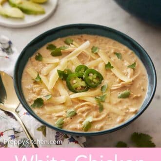 Pinterest graphic of a bowl of white chicken chili with shredded cheese, sliced jalapeno, and chopped cilantro on top. Sliced limes in the background.