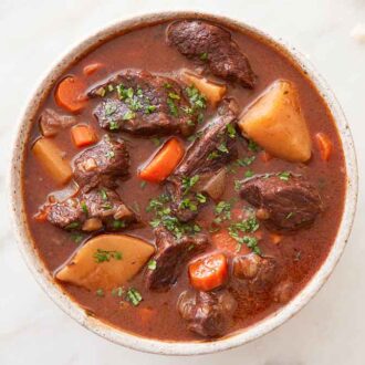 Overhead view of a bowl of beef stew with some torn bread off to the side.