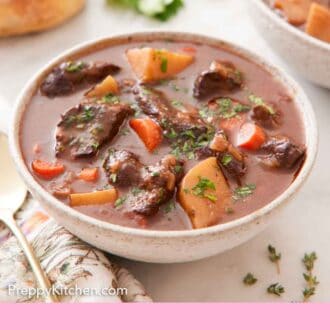 Pinterest graphic of a bowl of beef stew with a loaf of bread, herbs, and a second bowl off to the side.
