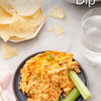 Pinterest graphic of a plate of buffalo chicken dip with two celery sticks with a plate of chips and glass of water in the background.