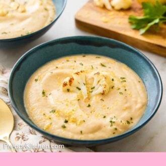 Pinterest graphic of a bowl of cauliflower soup with a cutting board with garnishes in the background with a second bowl of soup.