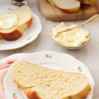 Pinterest graphic of a slice of challah on a plate with another plated slice, a bowl of butter, and a sliced loaf in the background.