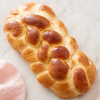 Overhead view of a loaf of challah with a pink linen beside it.