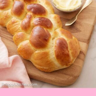 Pinterest graphic of a loaf of challah on a wooden serving board with a bowl of butter beside it.