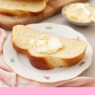 Pinterest graphic of a plate with a slice of challah with butter. A cut loaf and bowl of butter in the back.