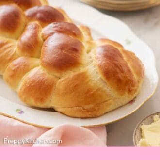 Pinterest graphic of a platter with a loaf of challah bread with a stack of palates in the background.