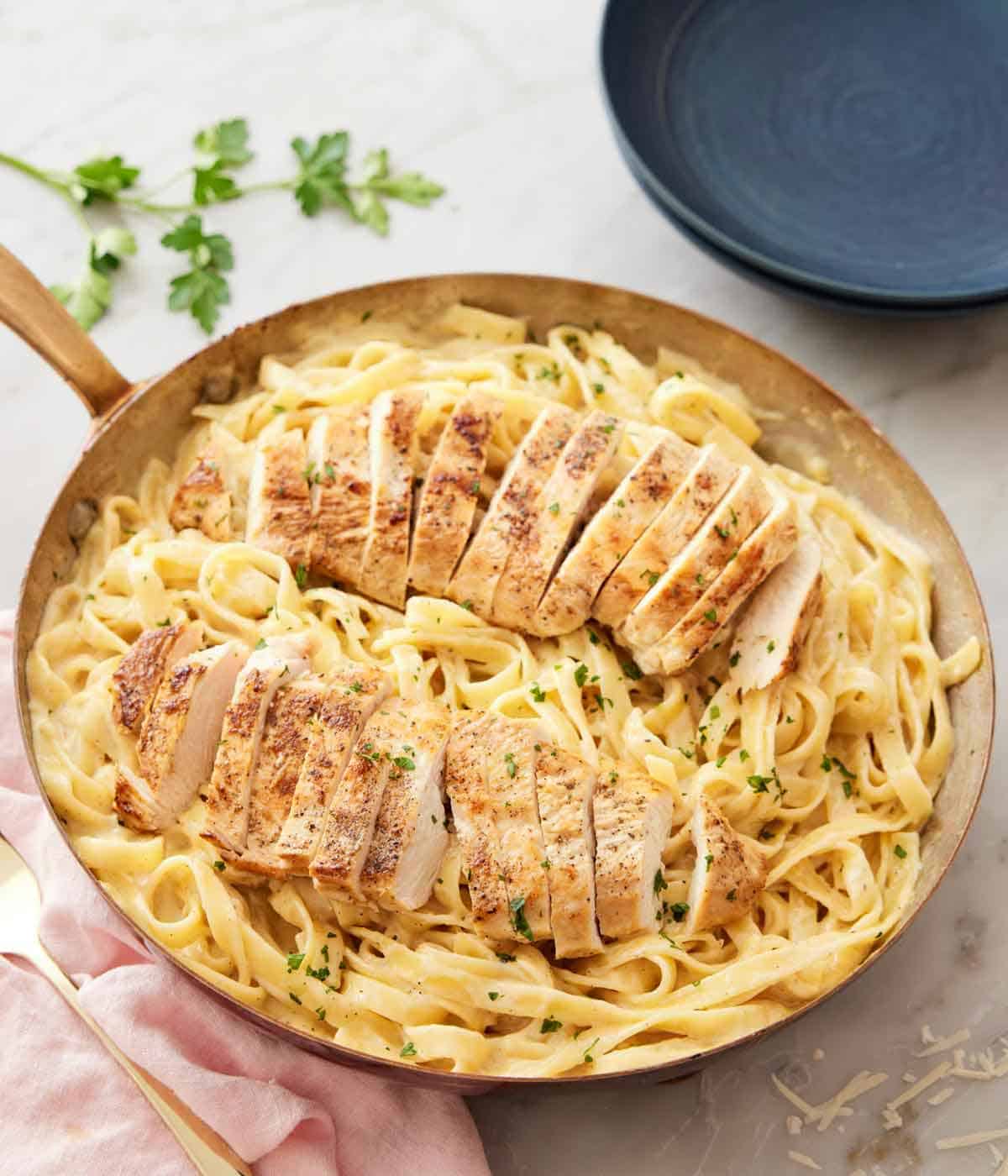 A skillet with chicken alfredo with two sliced chicken breasts over fettuccine noodles.