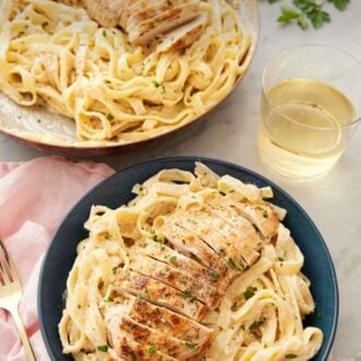 Pinterest graphic of a bowl of chicken alfredo with a glass of wine and skillet with more chicken alfredo behind it.