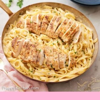 Pinterest graphic of a skillet of chicken alfredo with two sliced chicken breasts on top.