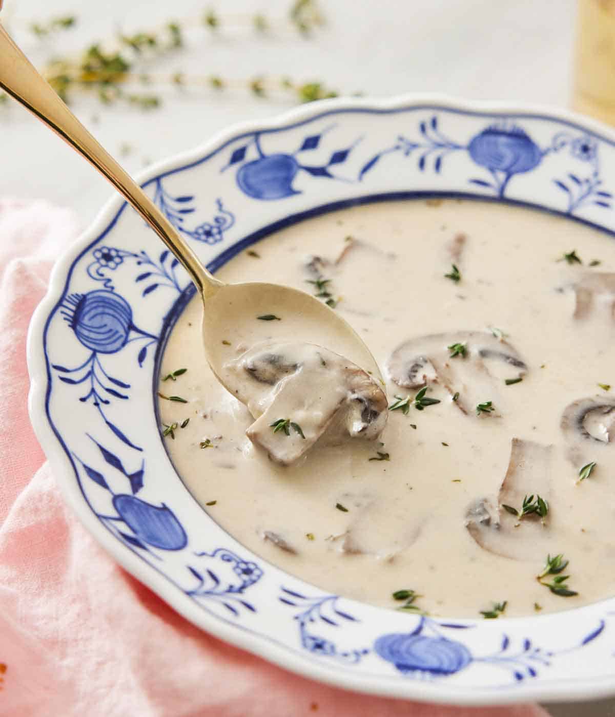 Close up of a bowl of cream of mushroom soup with a spoonful lifted up.