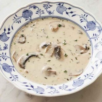 A bowl of cream of mushroom soup with fresh thyme garnishing the soup and more in the background.
