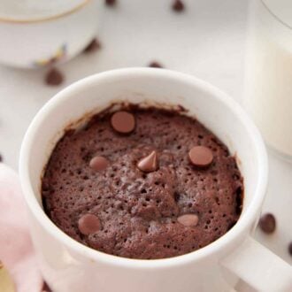 Pinterest graphic of a mug cake with a glass of milk and bowl of whipped cream in the back.