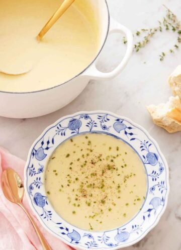 A bowl of potato leek soup with garnish with a large pot of soup with a ladle in the background.