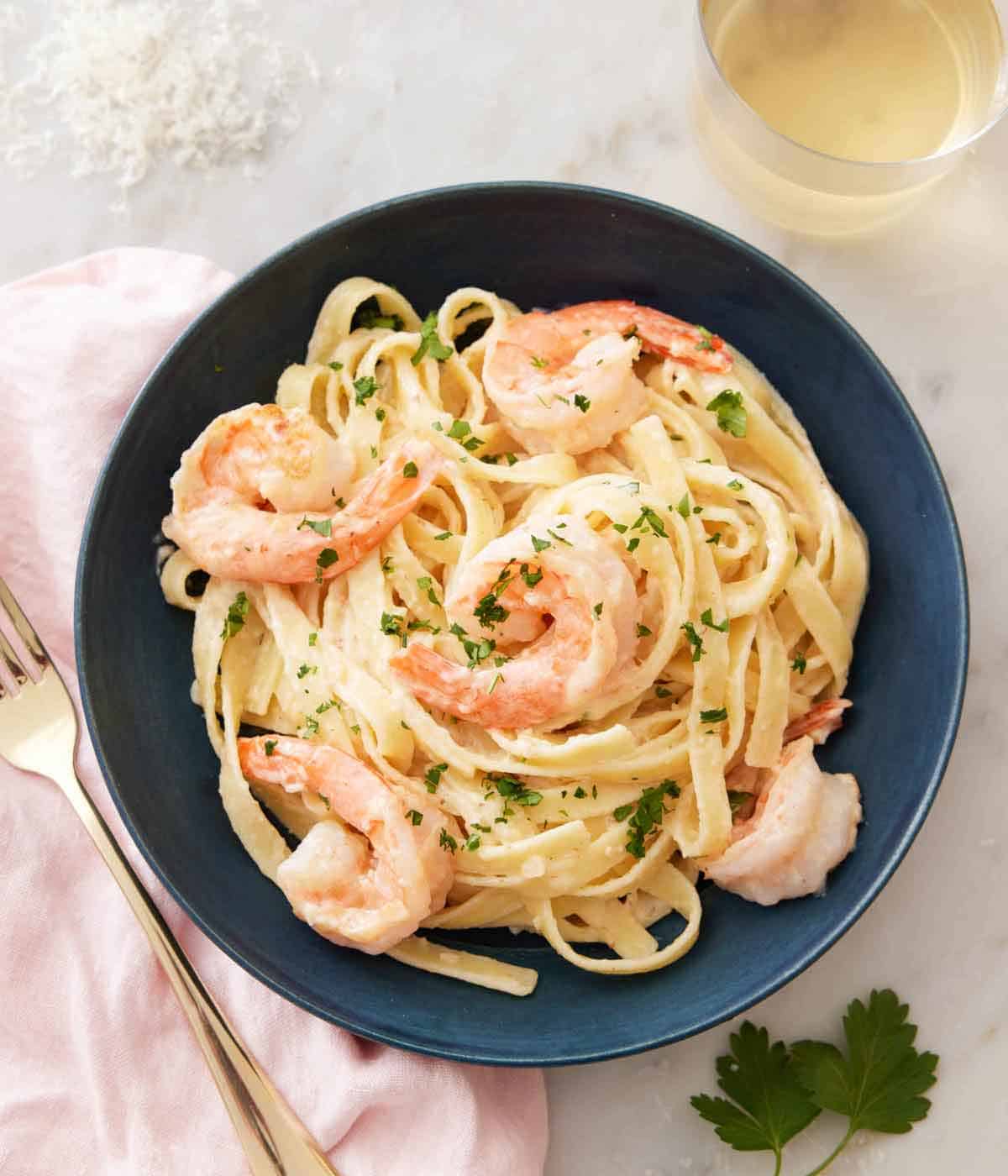 Overhead view of a plate of shrimp Alfredo pasta with a fork and glass of wine beside it.