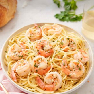 Pinterest graphic of a plate of pasta with shrimp scampi on top with bread, parsley, and wine in the background.