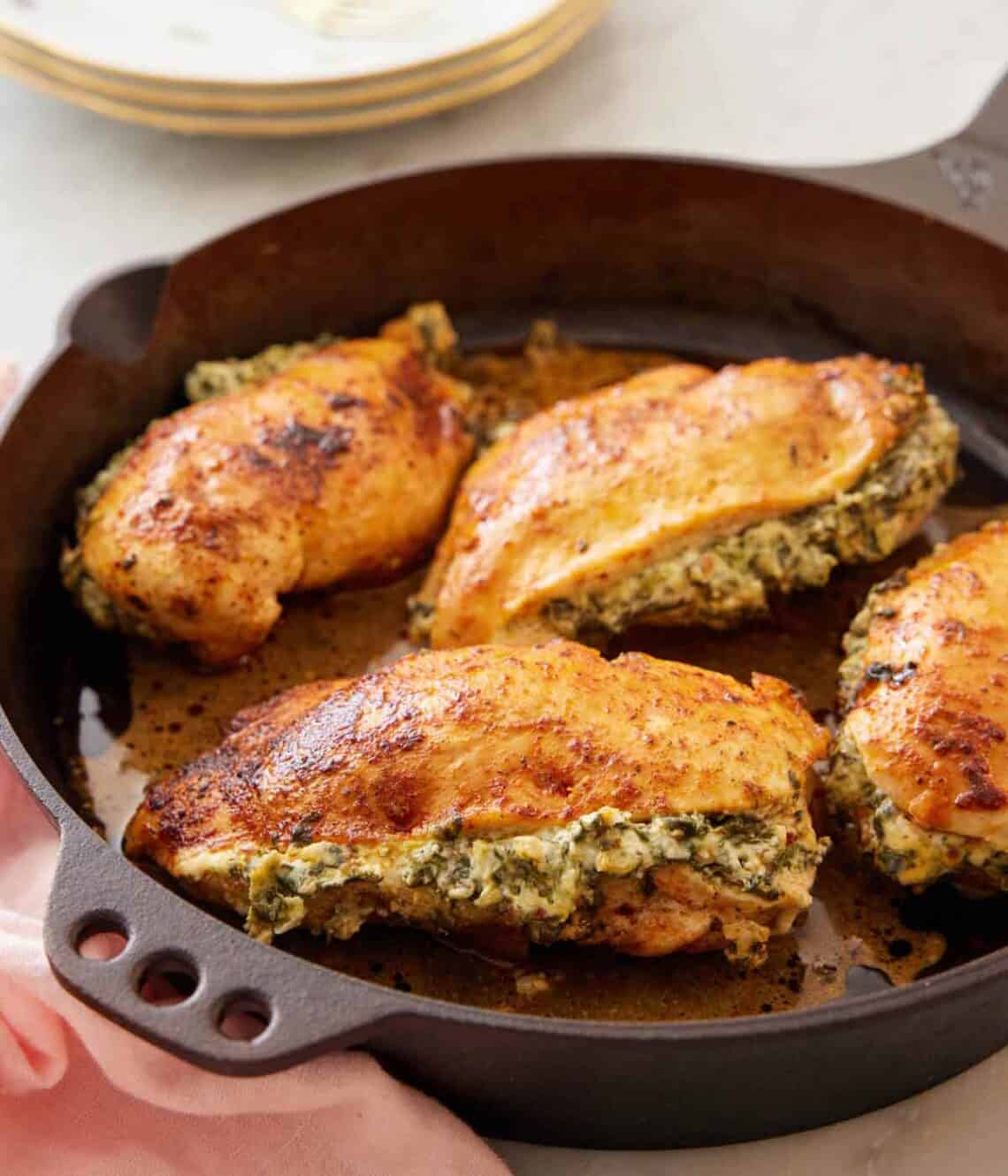 A cast iron skillet with four spinach stuffed chicken breasts.