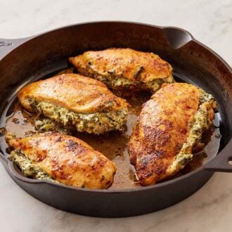 A cast iron skillet with four spinach stuffed chicken breasts with a pink linen off to the side.