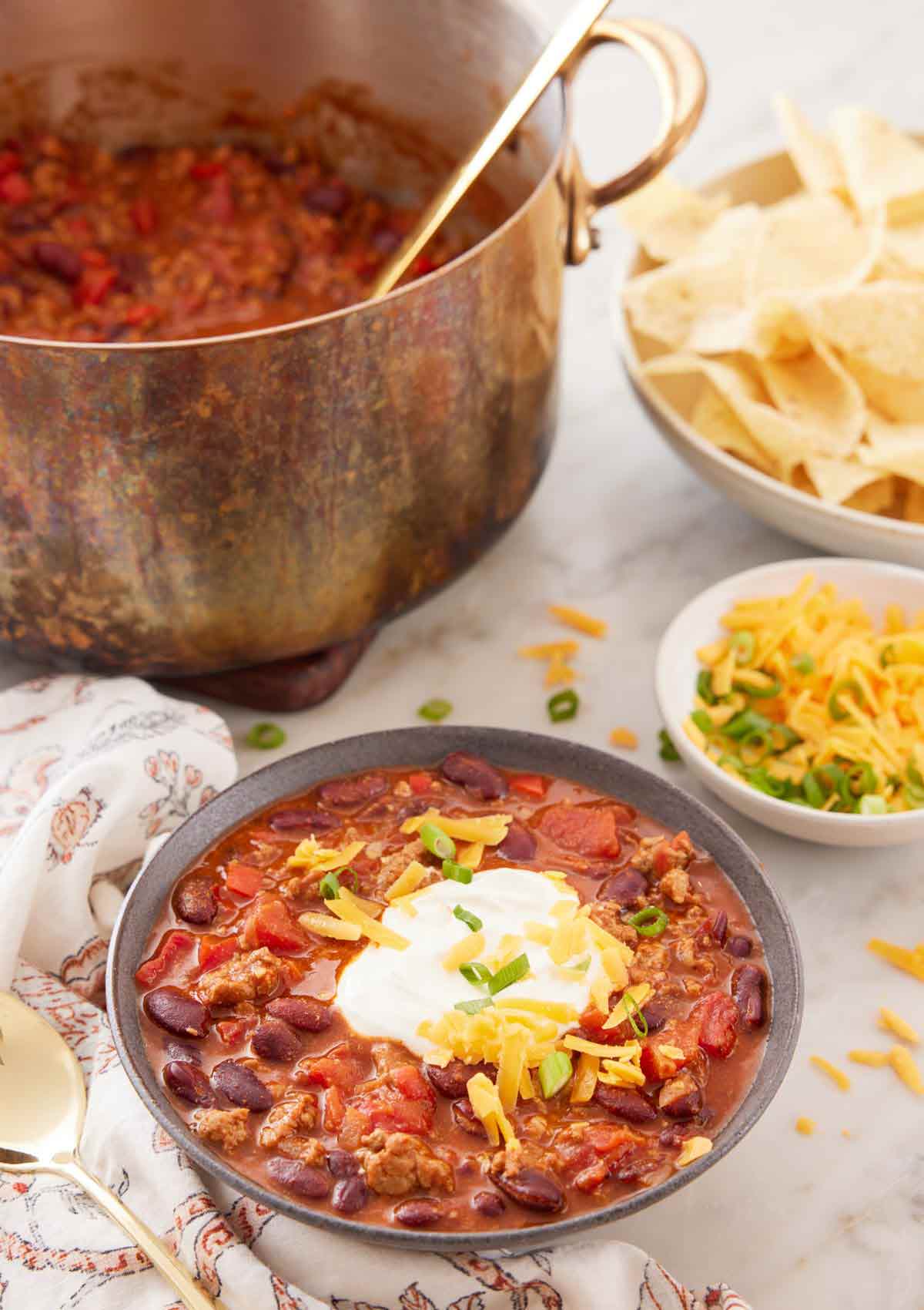 A bowl of turkey chili with bowls of toppings and a pot of more chili in the background.