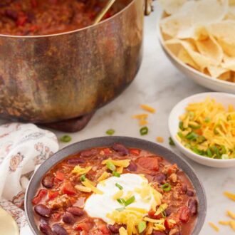 Pinterest graphic of a bowl of turkey chili with a pot with more chili and bowls of toppings in the background.